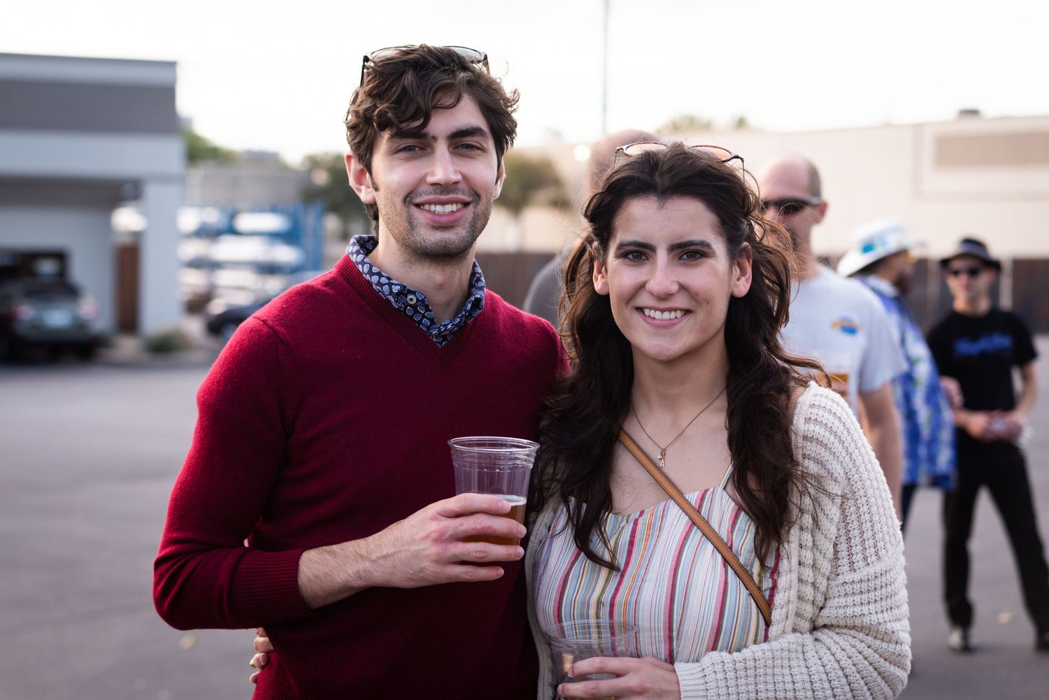 Two people smile while enjoying drinks at outdoor social gathering.