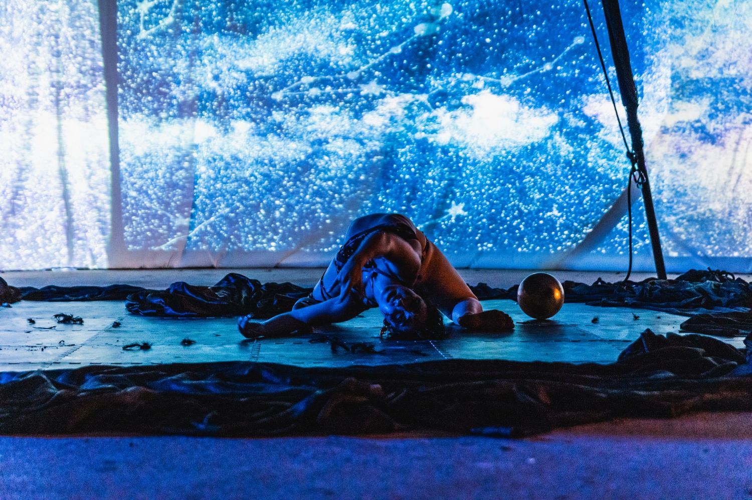 Athletic performer in graceful floor movement against starlit projection screen.
