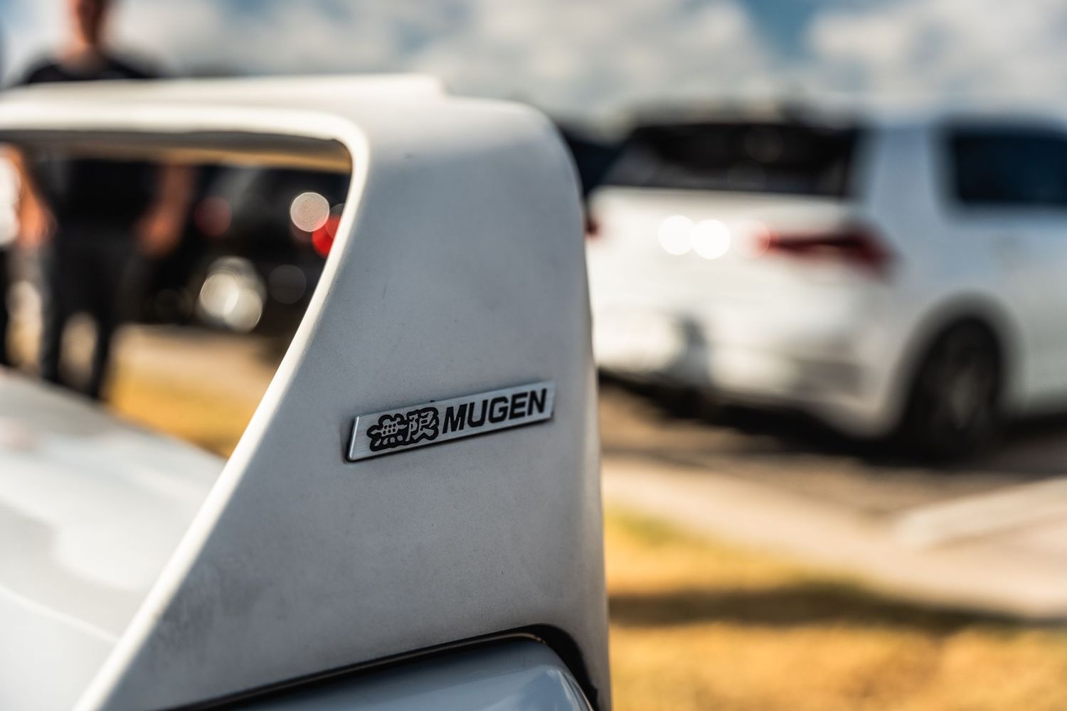 Close-up detail shot of a Mugen badge on a white vehicle panel.