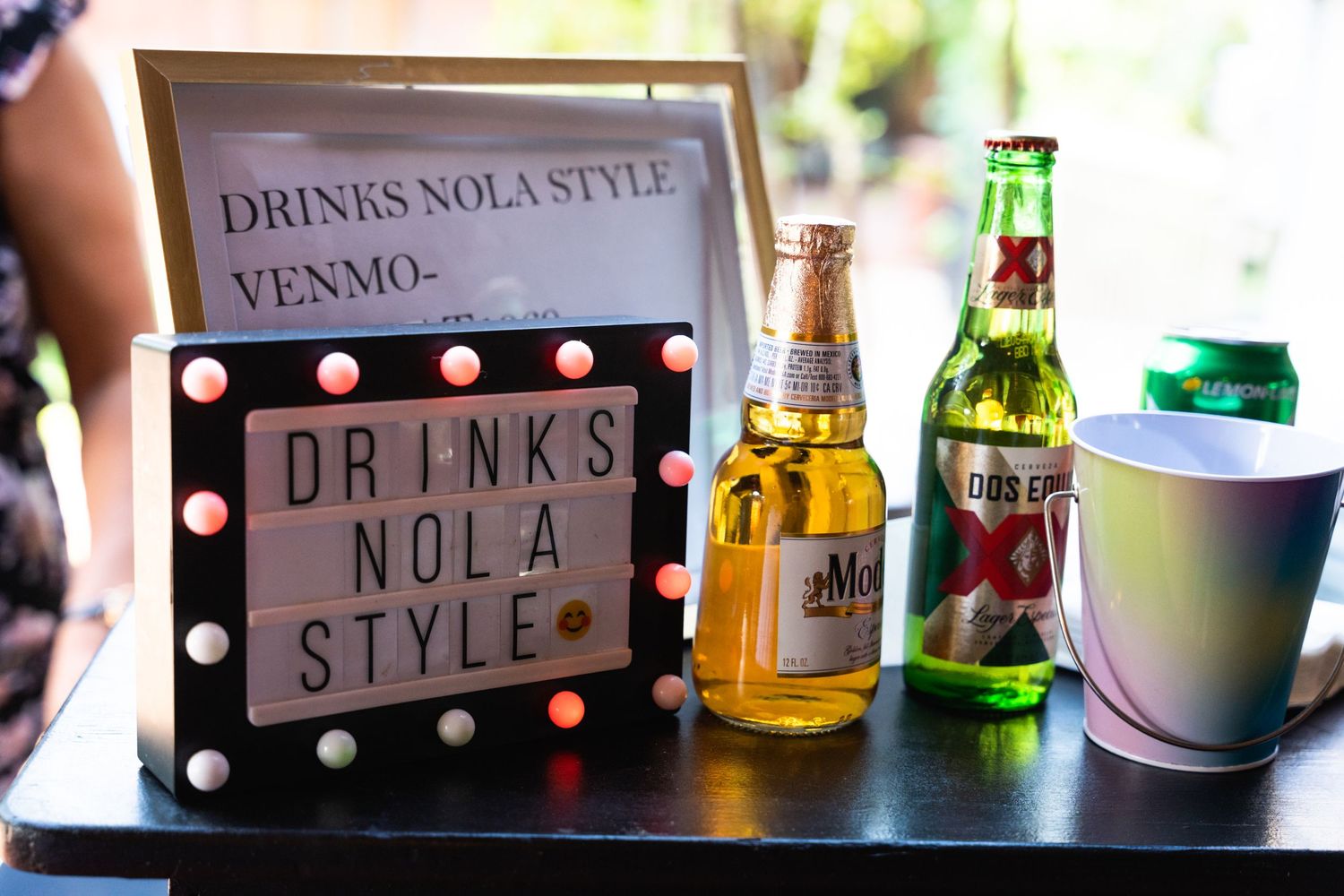 Drinks station with illuminated sign reading 'Drinks NOLA Style' and assorted beverages on display.