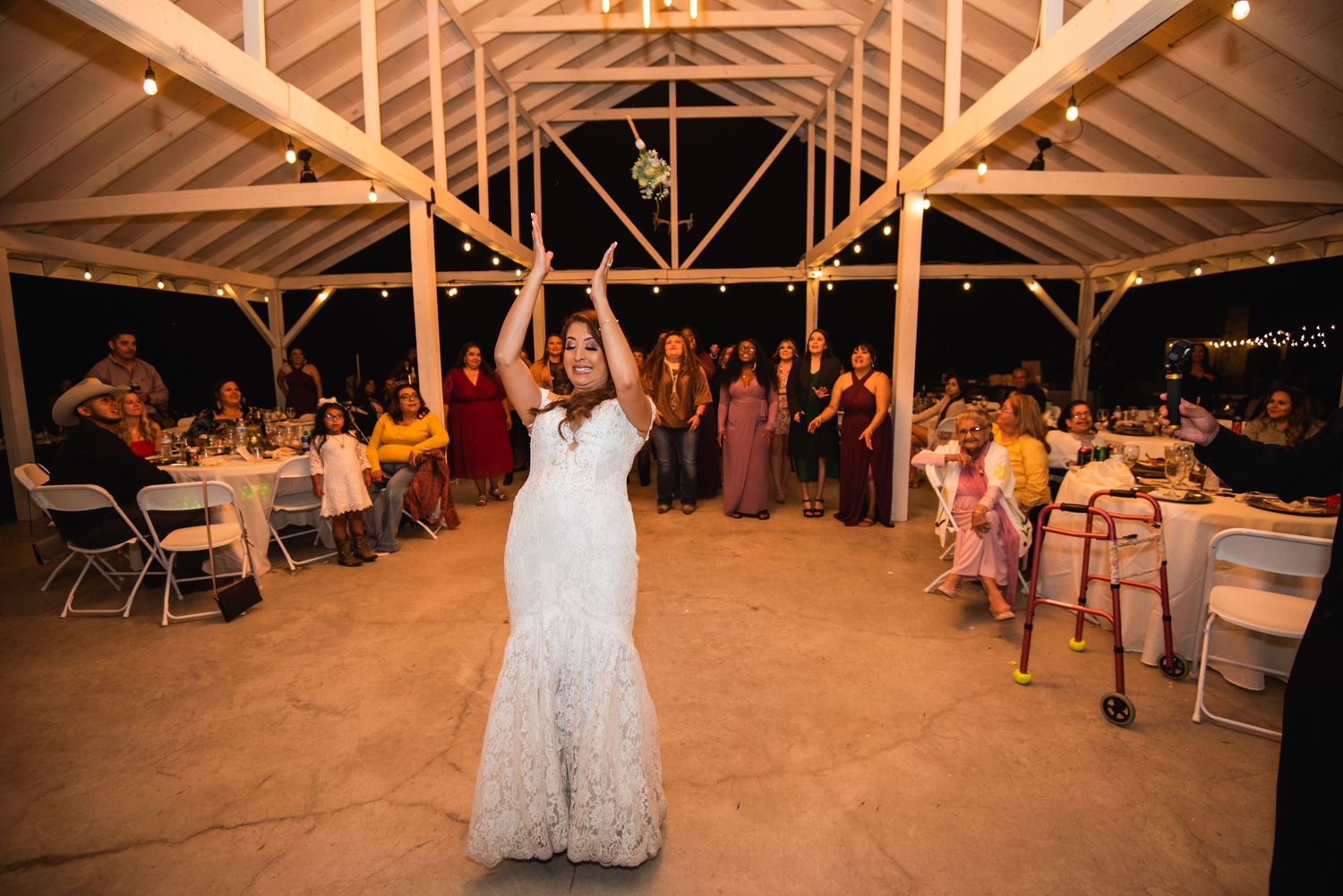 A wedding celebration in a wooden barn venue with guests gathered around tables and dancing.