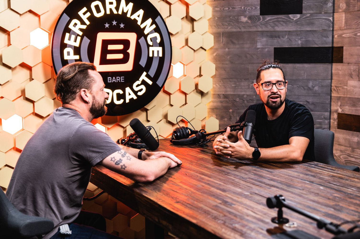Two people recording a podcast in a studio with hexagonal wall decorations.