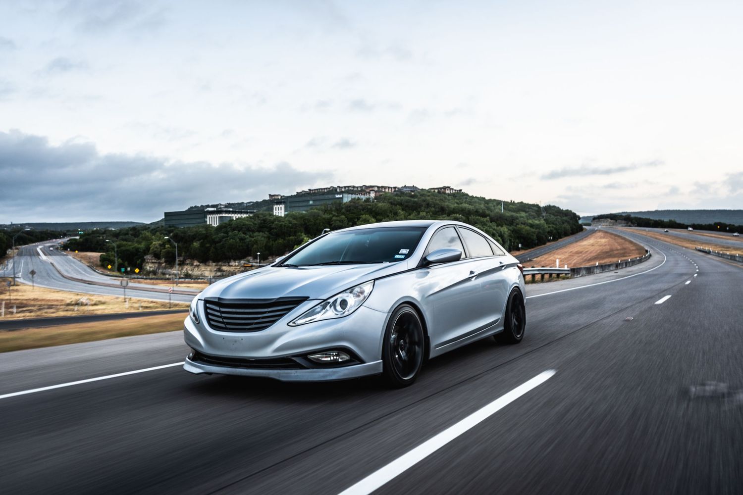 Silver Hyundai Sonata with sport modifications photographed on a curved mountain road.