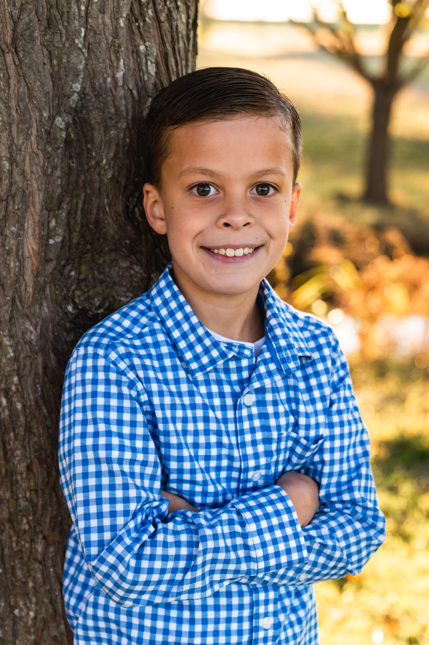 Portrait against tree trunk wearing blue gingham shirt in autumn setting.