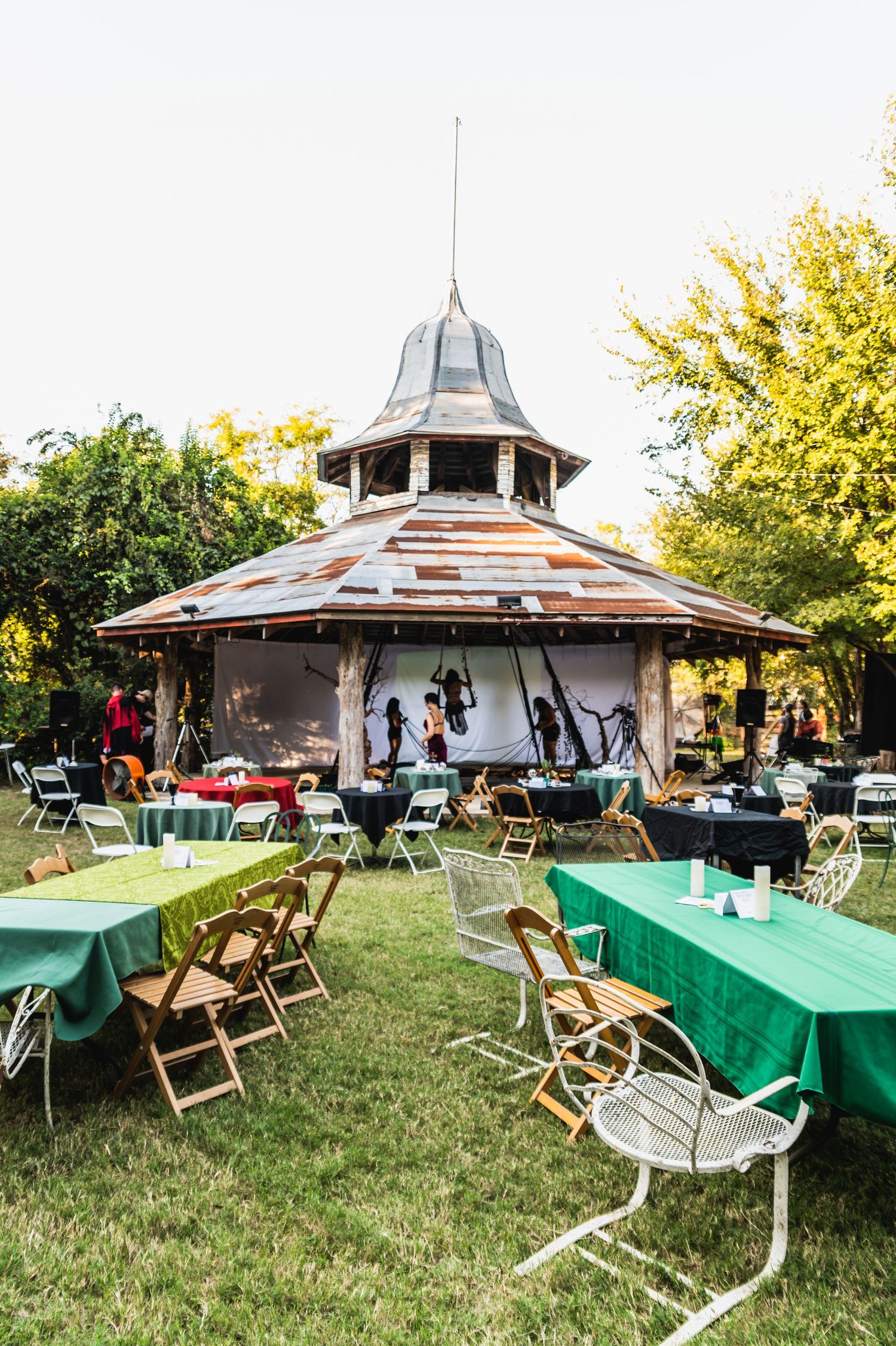 Octagonal gazebo setup with green tablecloths and folding chairs for outdoor event.