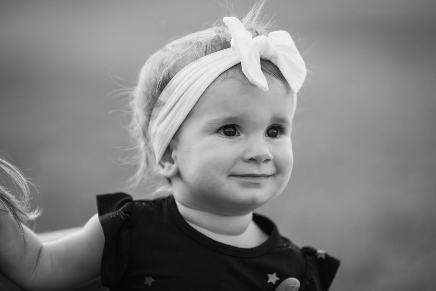 Black and white portrait of a small child wearing a white bow headband.