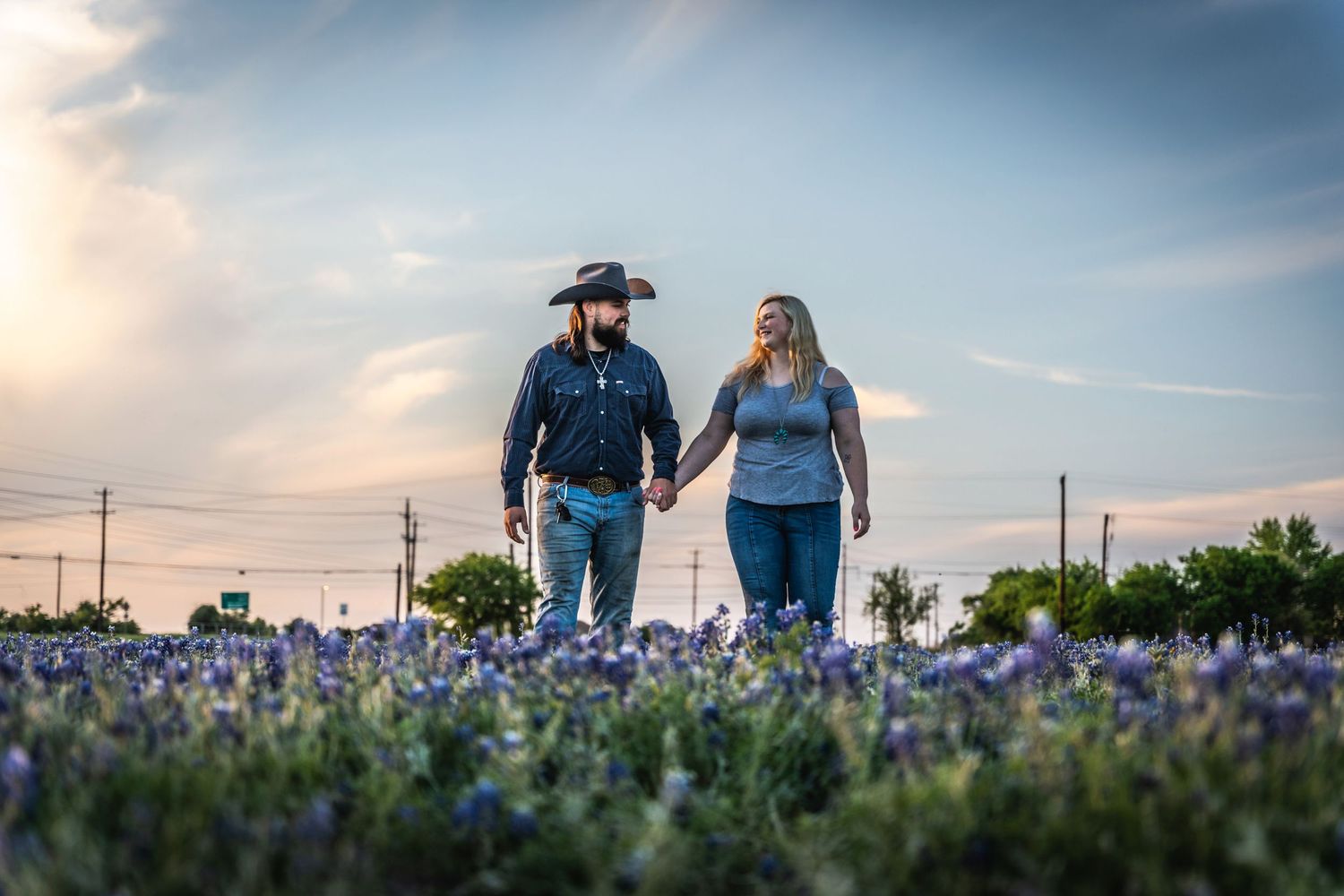 A couple walks hand in hand through a field of bluebonnets at sunset.