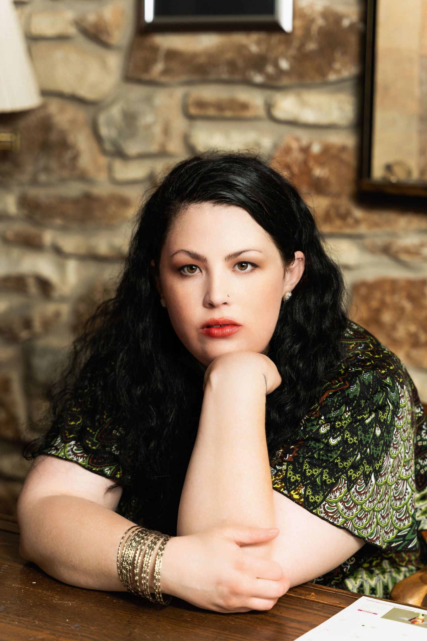 Classic portrait against stone wall featuring dark hair and green patterned dress.