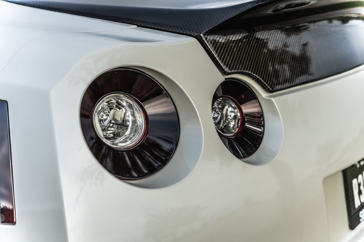 Close-up detail shot of circular LED taillights on white sports car.