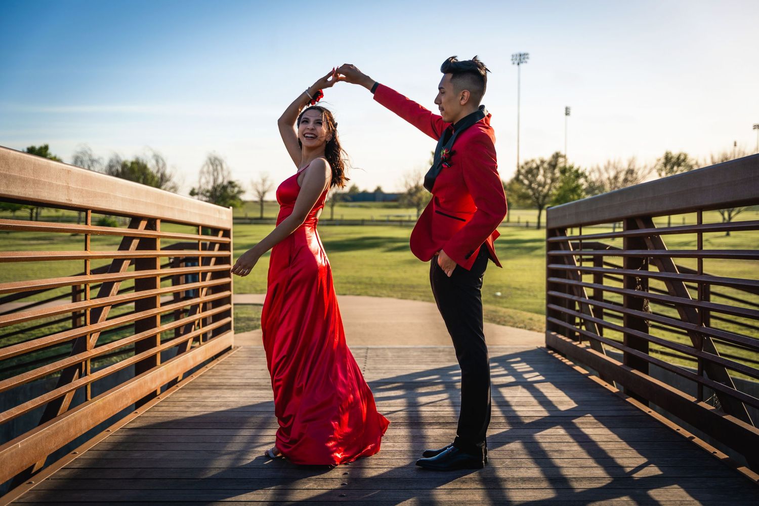 Couple dancing on a wooden bridge at sunset, with red dress flowing in motion.