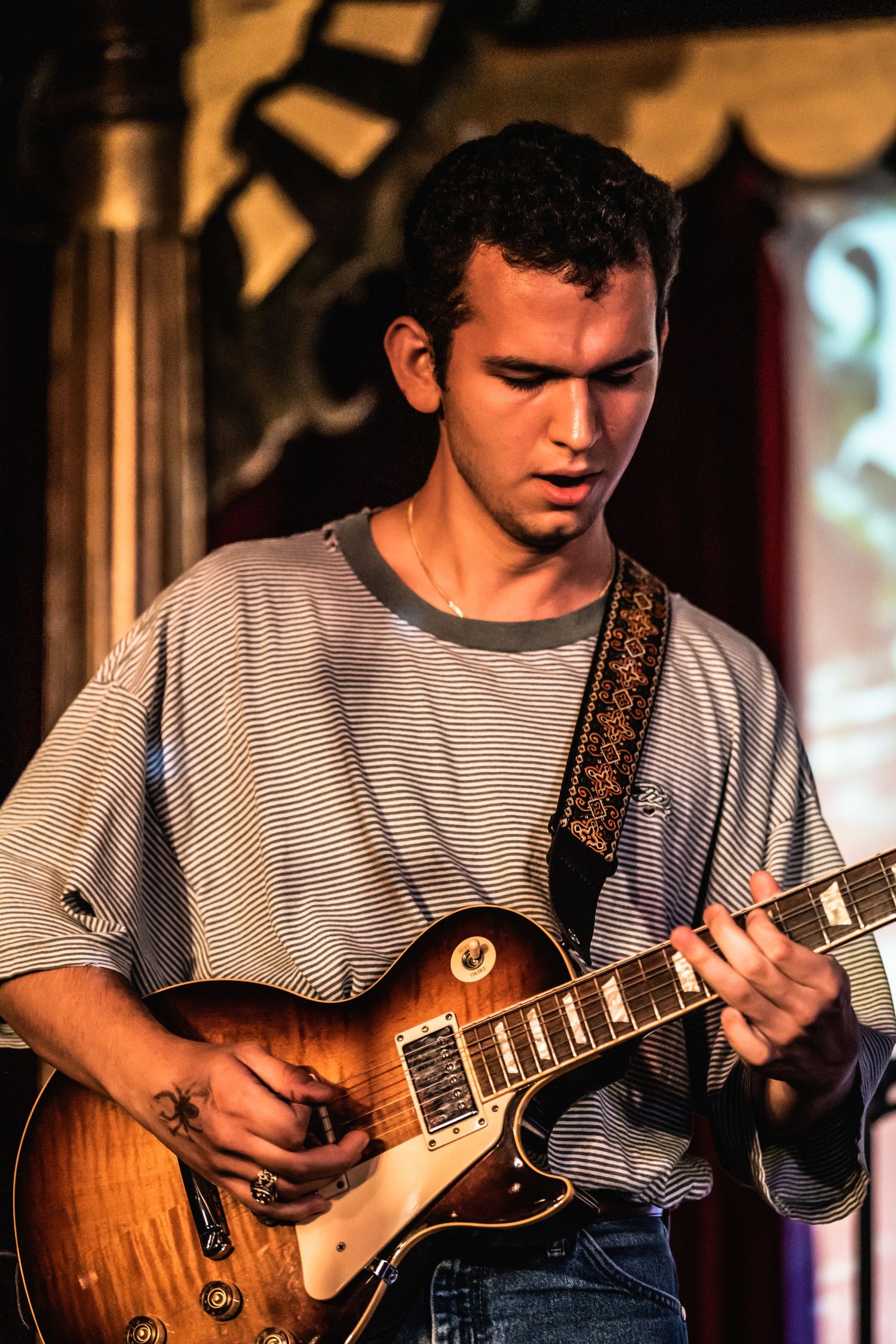 Guitarist performing on stage with a vintage Les Paul guitar under dramatic lighting.