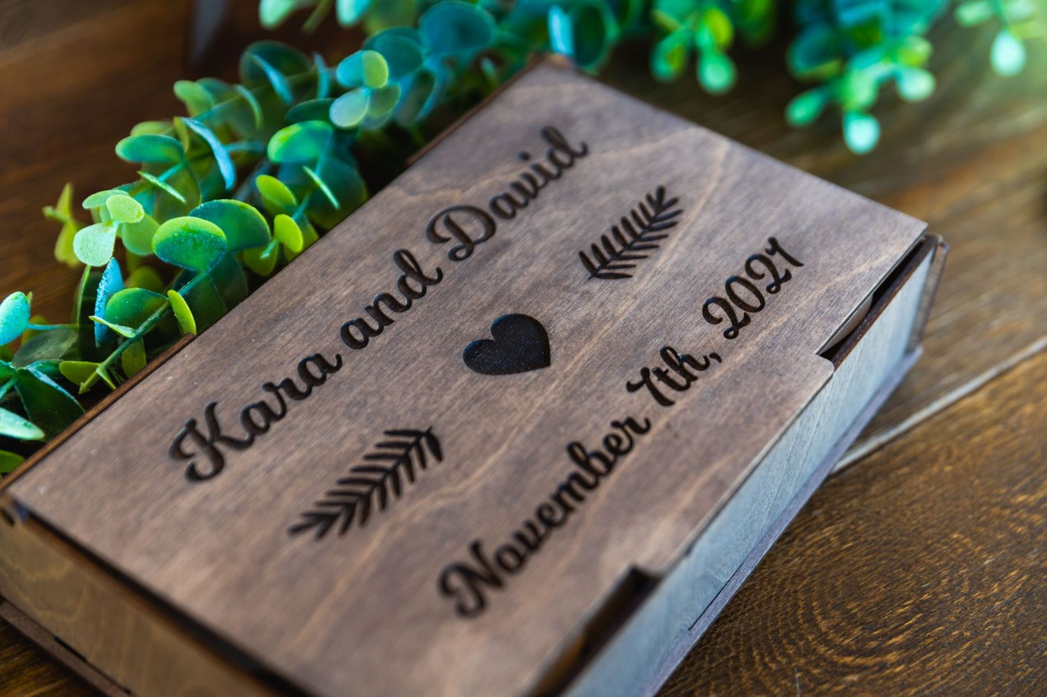 Wooden wedding album cover with names and arrows engraved on dark wood.