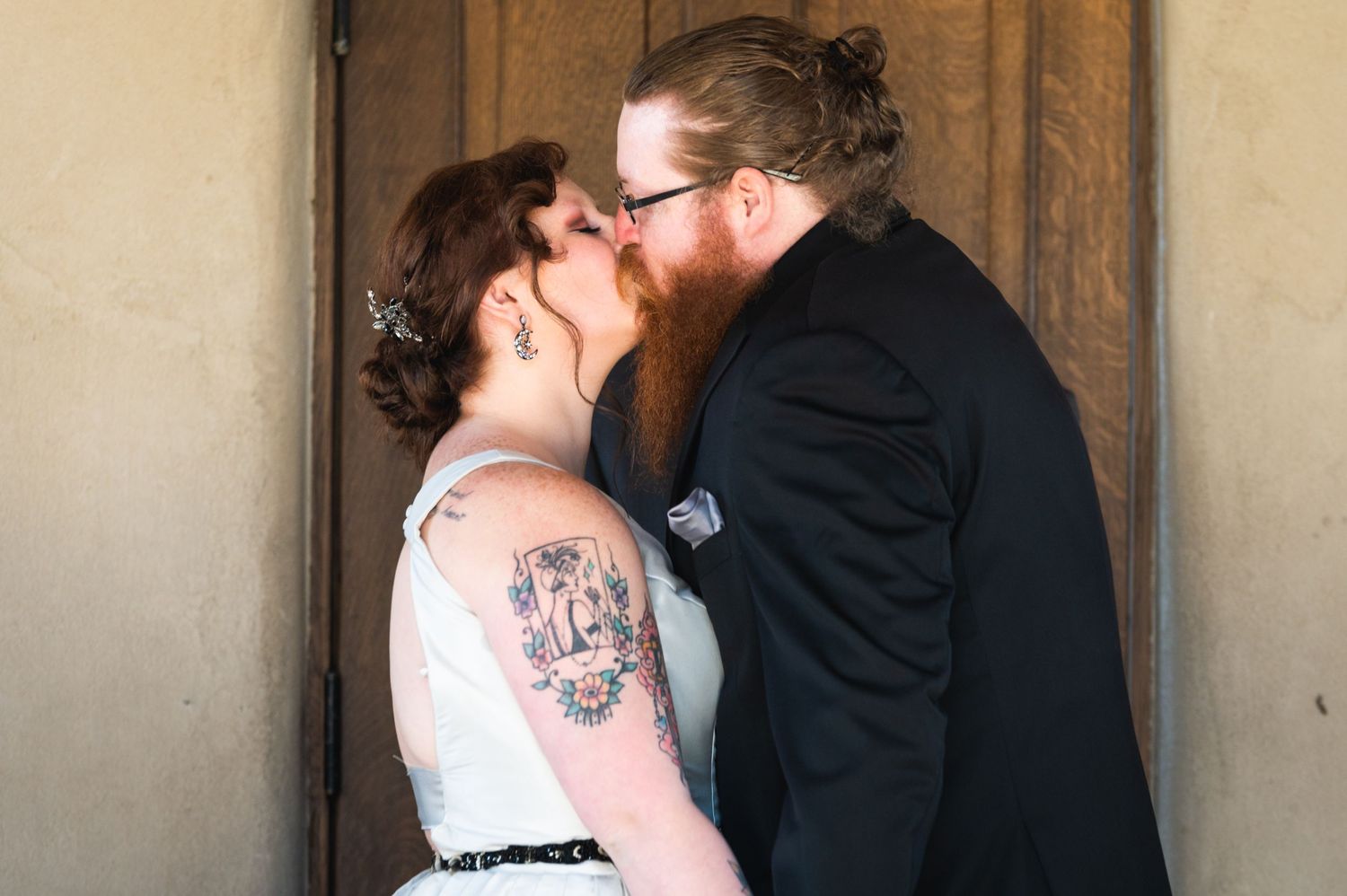 A romantic wedding kiss moment captured against a wooden door background.