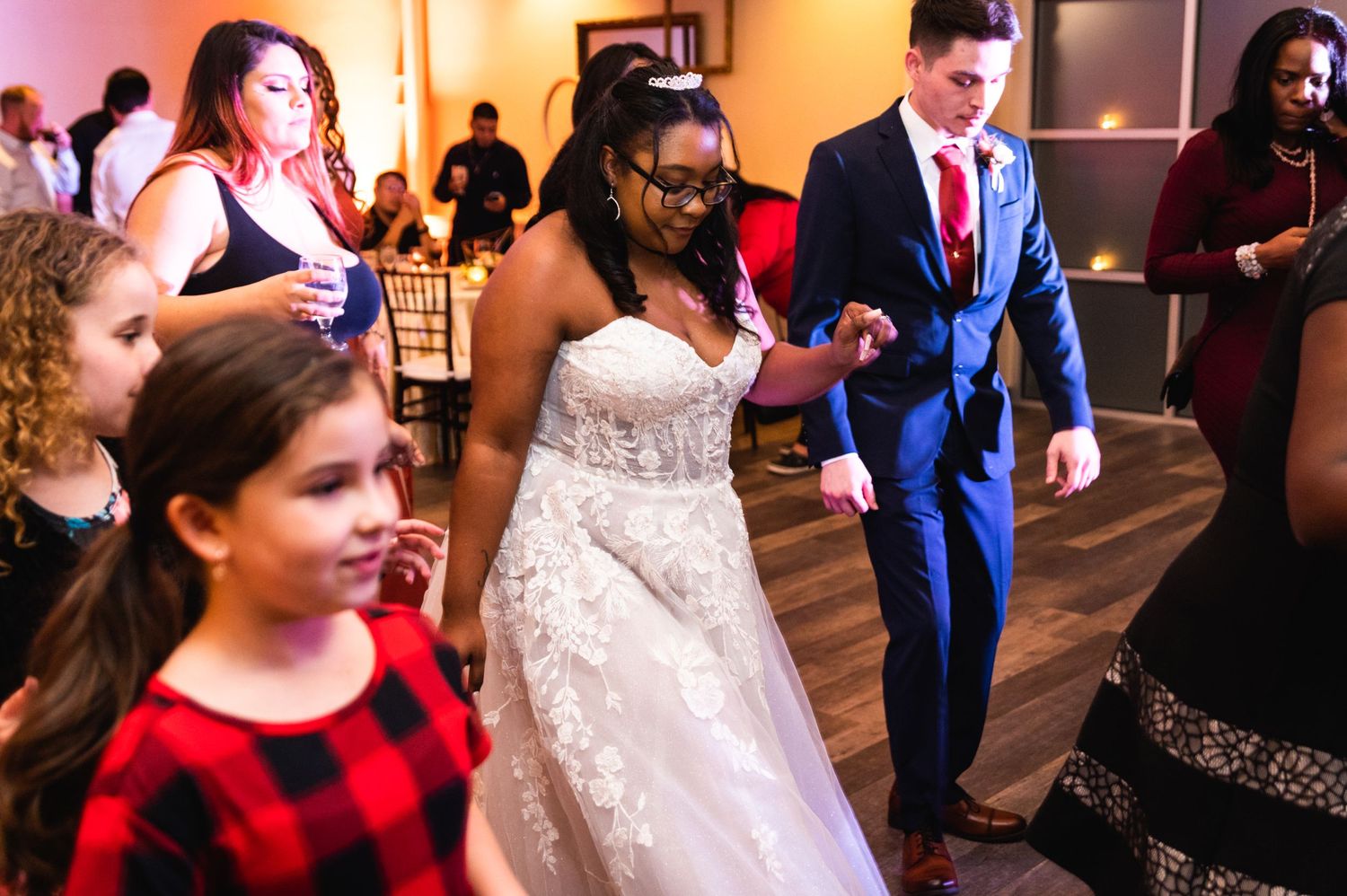 Wedding guests dancing together at a lively indoor reception with red lighting accents.