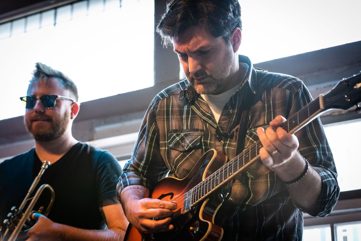 Two musicians performing together with guitars in a bright indoor space.