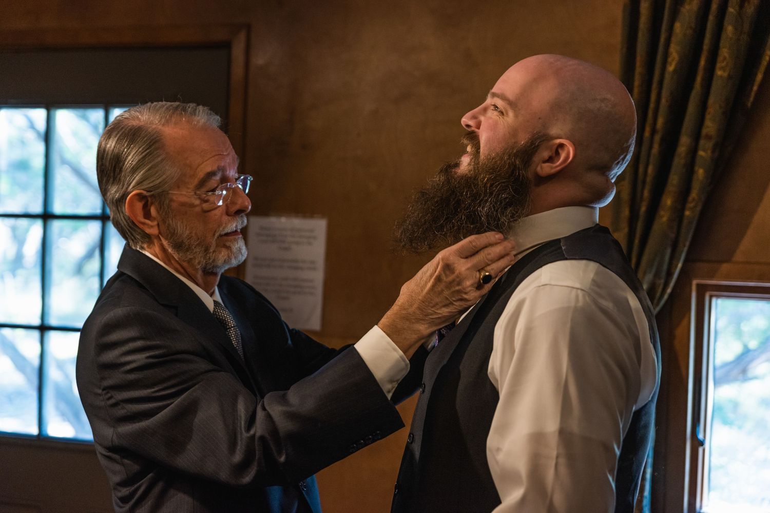Someone helps adjust another person's tie in a wood-paneled room.