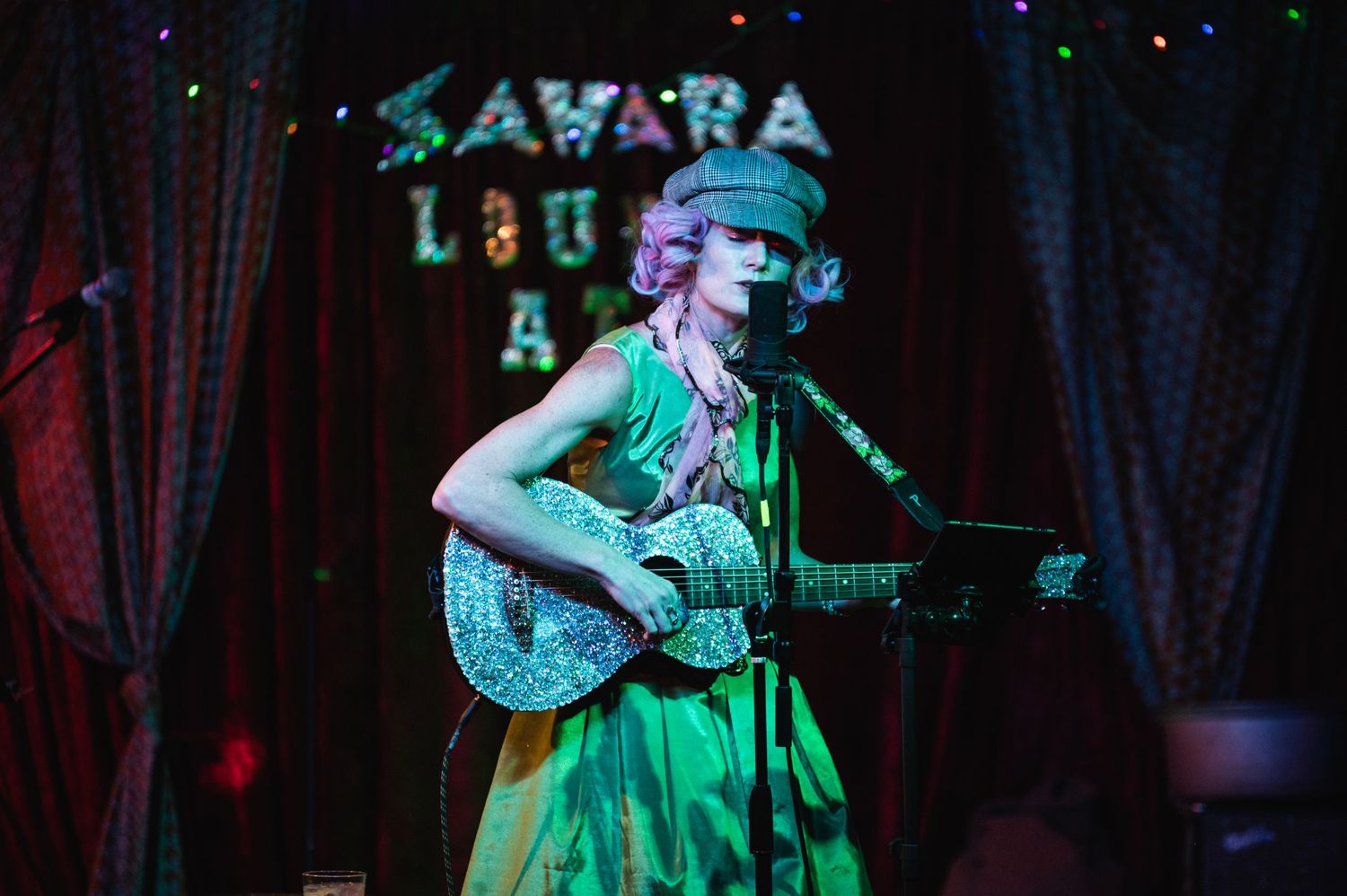 A performer plays guitar at the Sahara Lounge under green and purple stage lighting.