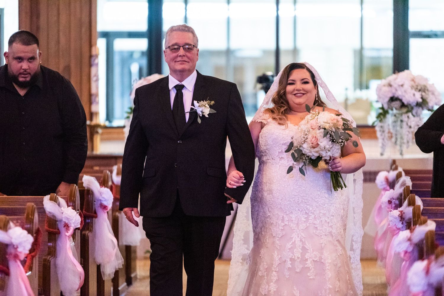 Wedding ceremony processional with pink floral decorations lining the church aisle.