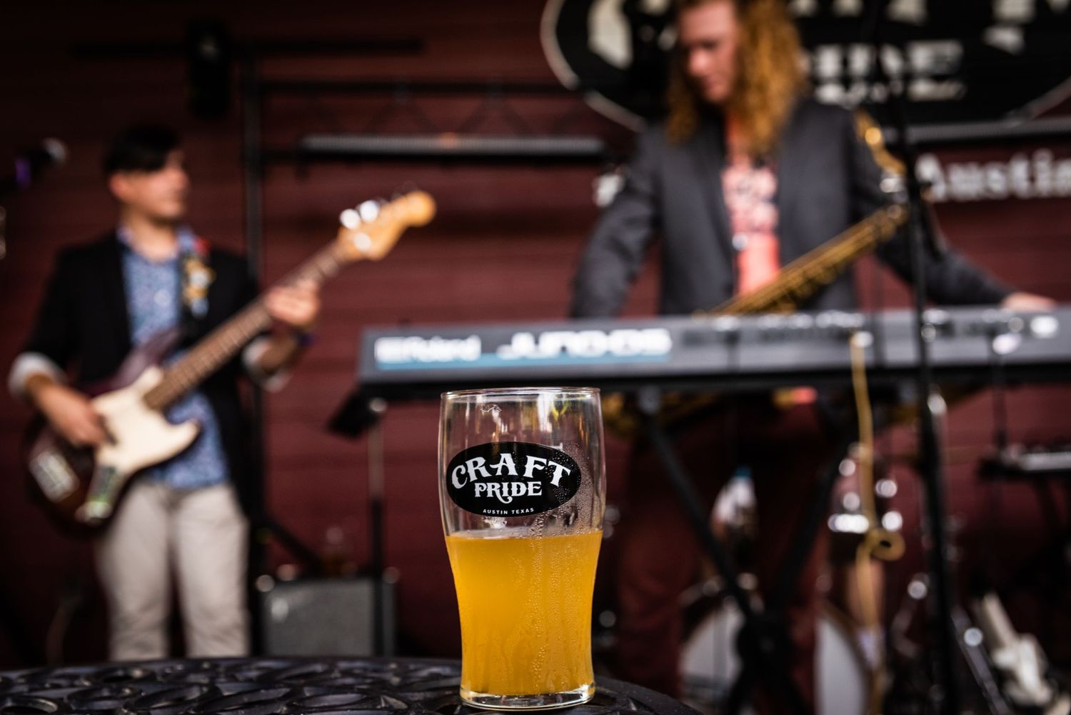 Glass of craft beer with musicians performing on stage in background.