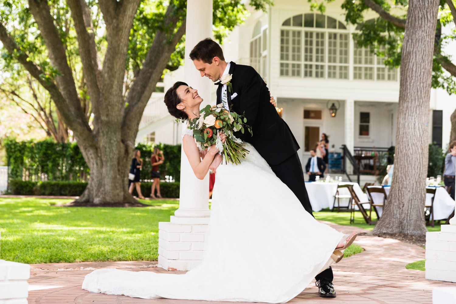 A romantic wedding dip pose on a garden patio with a white colonial style building in the background.
