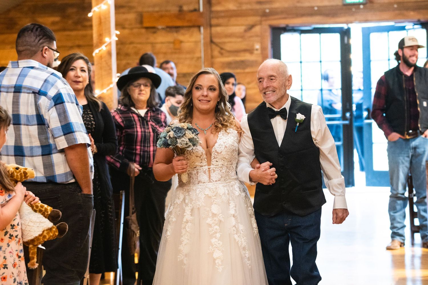 A wedding ceremony procession in a rustic wooden venue with guests looking on.