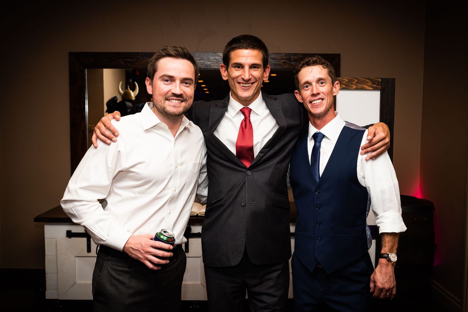 Three friends in formal attire pose together at an evening wedding celebration.