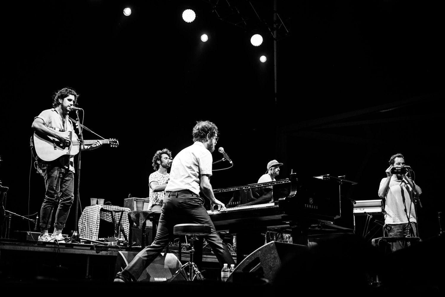 Black and white concert photo showing musicians performing on stage with guitars and keyboard under spotlights.
