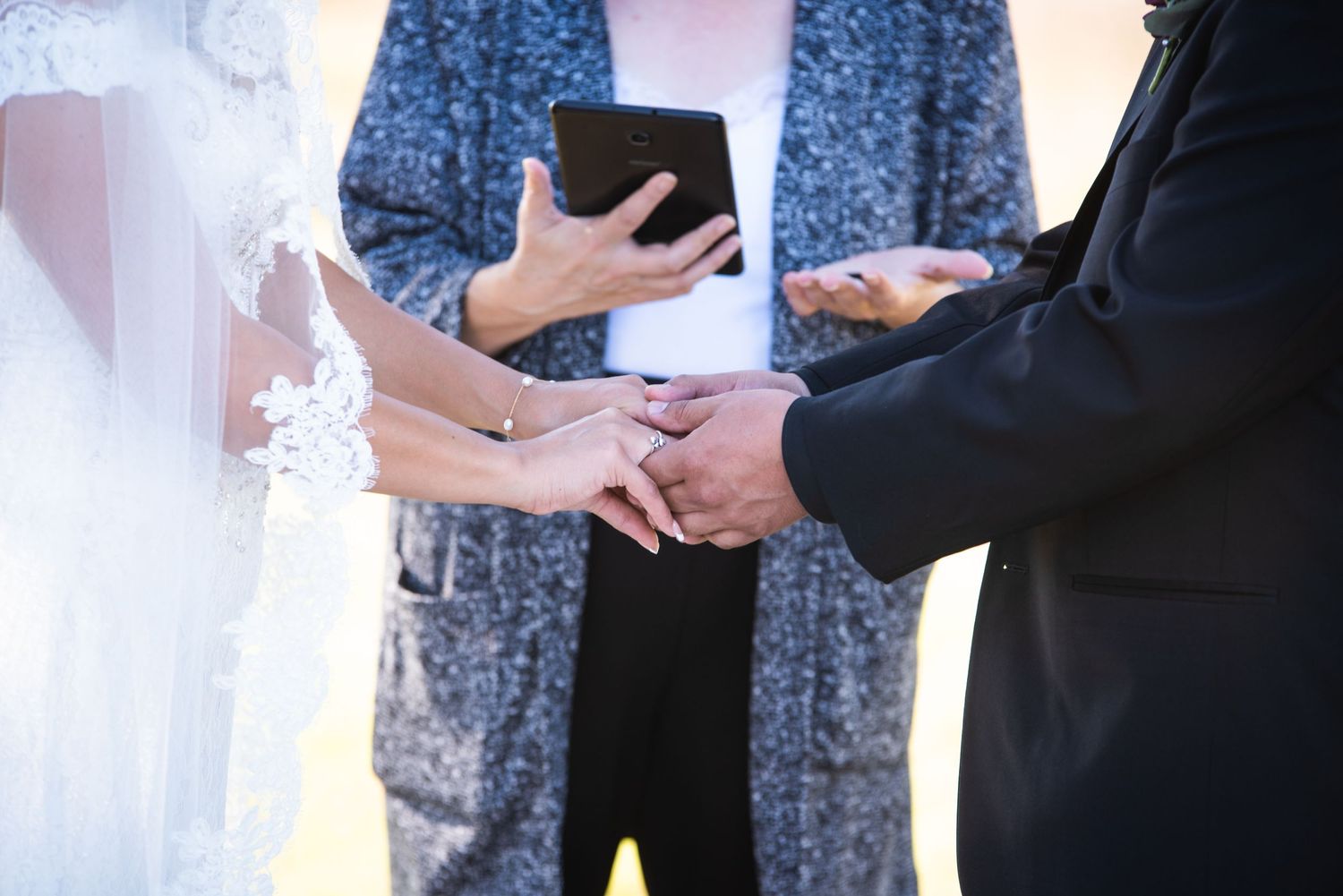 Close-up of hands during wedding ring exchange ceremony with officiant holding ceremony book.