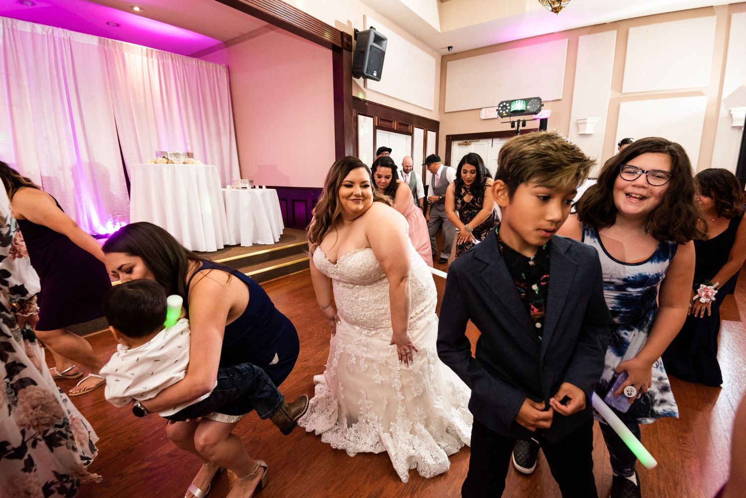 Wedding reception guests dancing and celebrating on the dance floor with pink lighting effects.