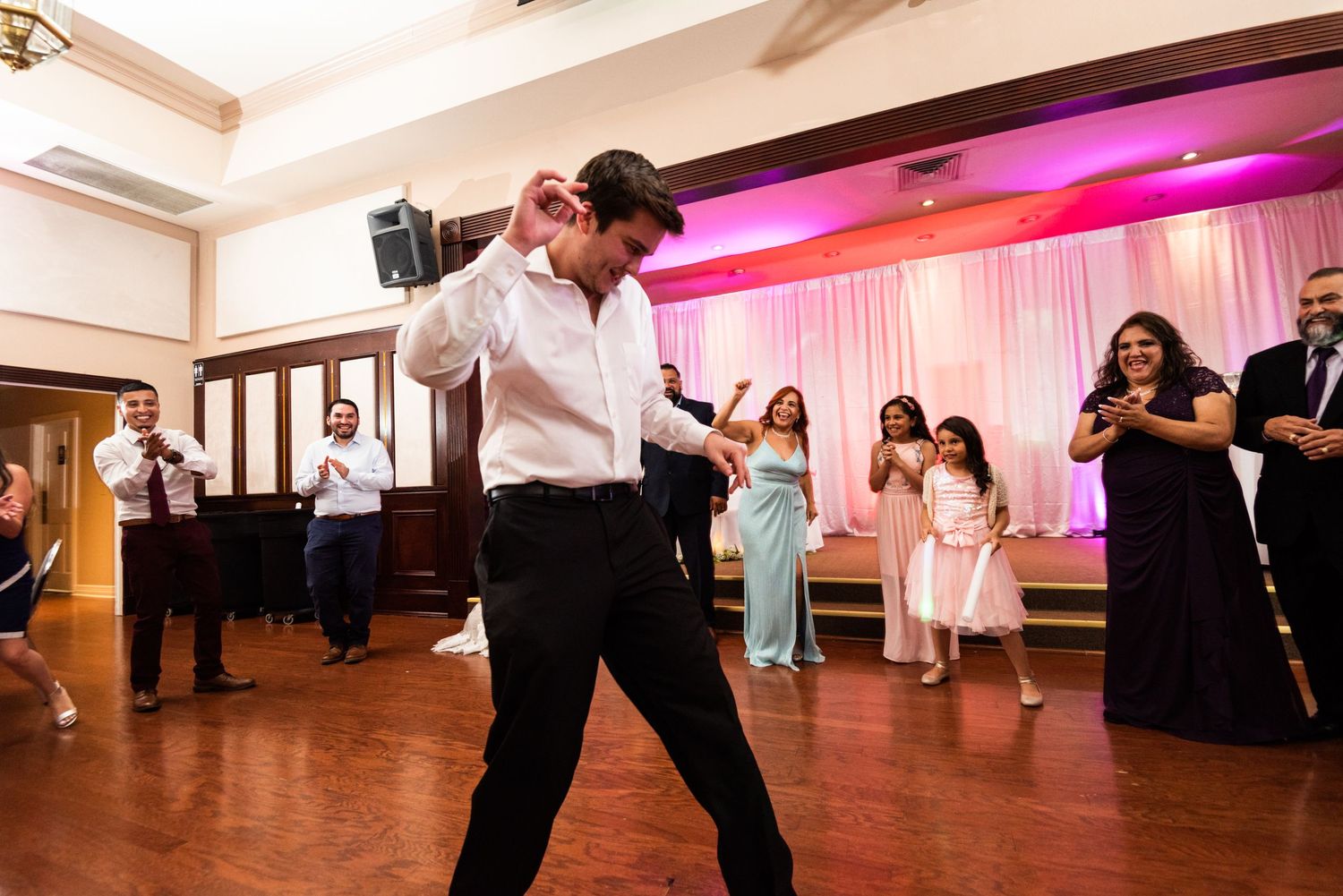 Guest performing energetic dance moves at reception while others watch in background.