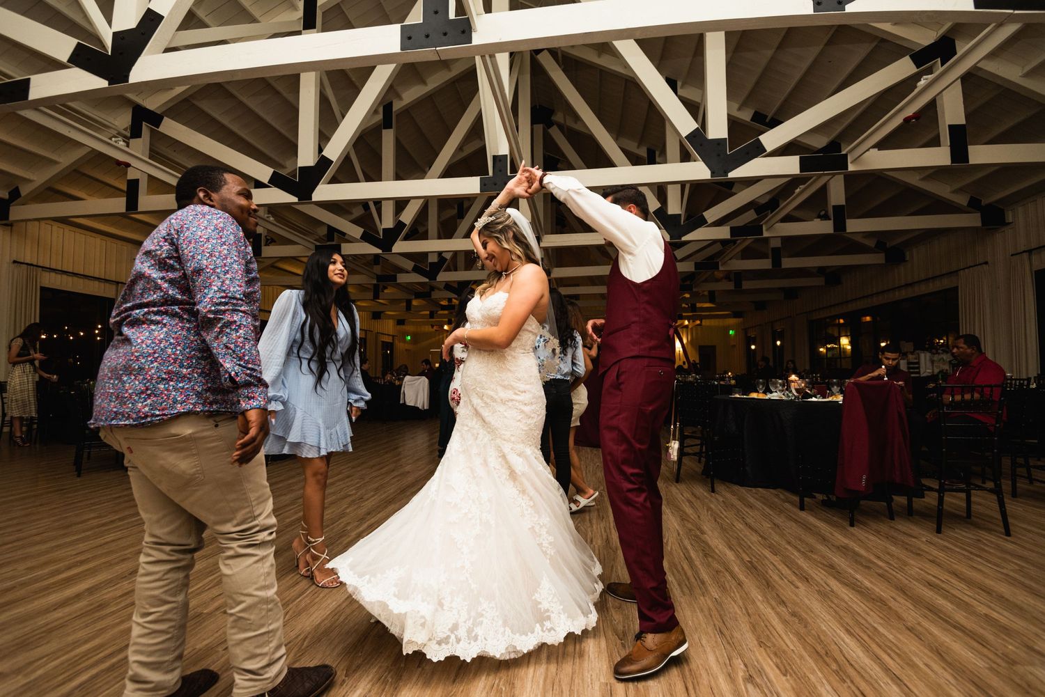 Celebration on the dance floor with bride in white gown and guests in burgundy attire.