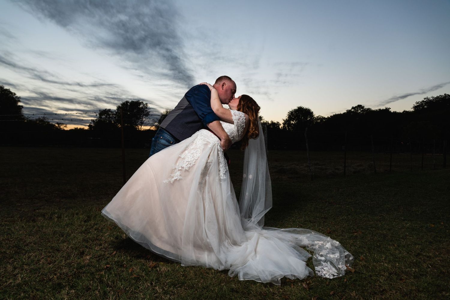 A couple shares their first kiss as newlyweds during sunset in a dramatic dip pose.