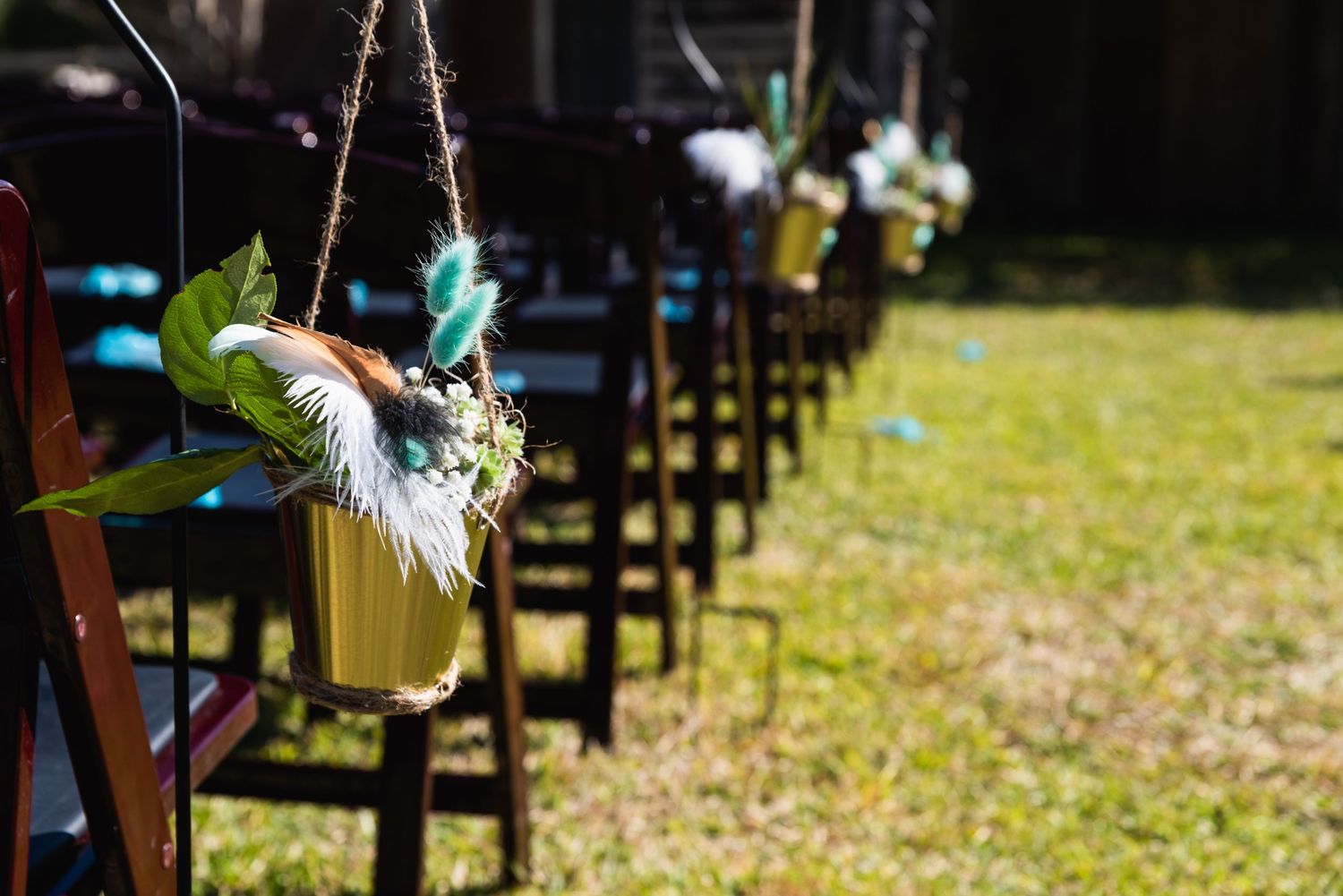 Mason jars with flowers hang from wooden stakes along an outdoor ceremony aisle.
