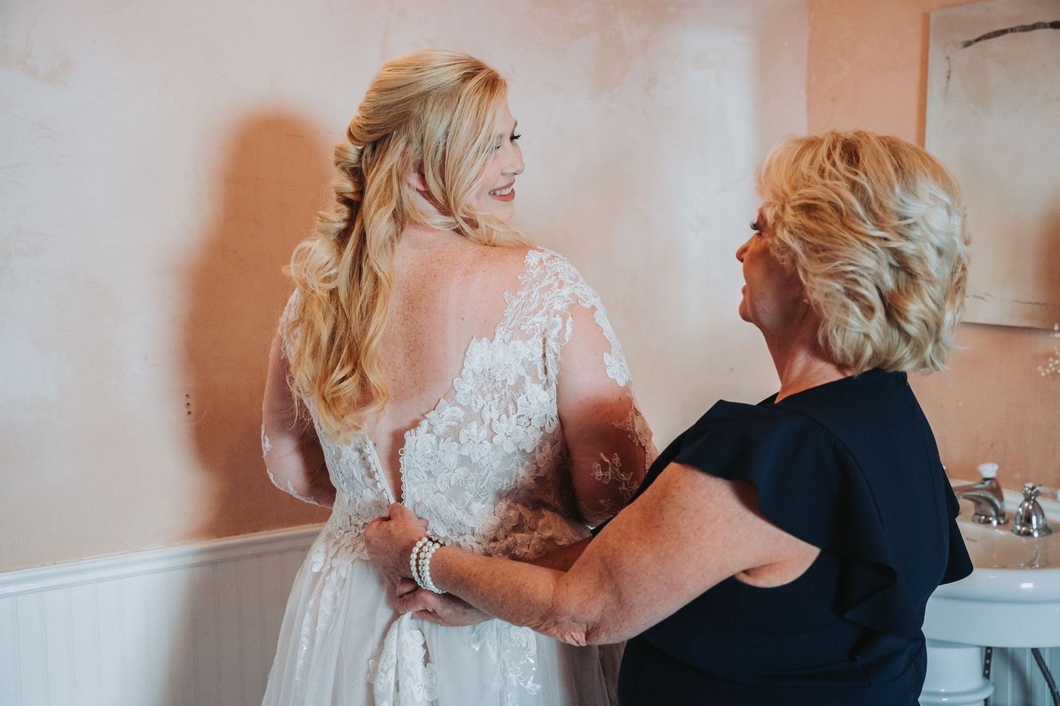 A heartwarming moment of dress preparation between two people in a bathroom setting.