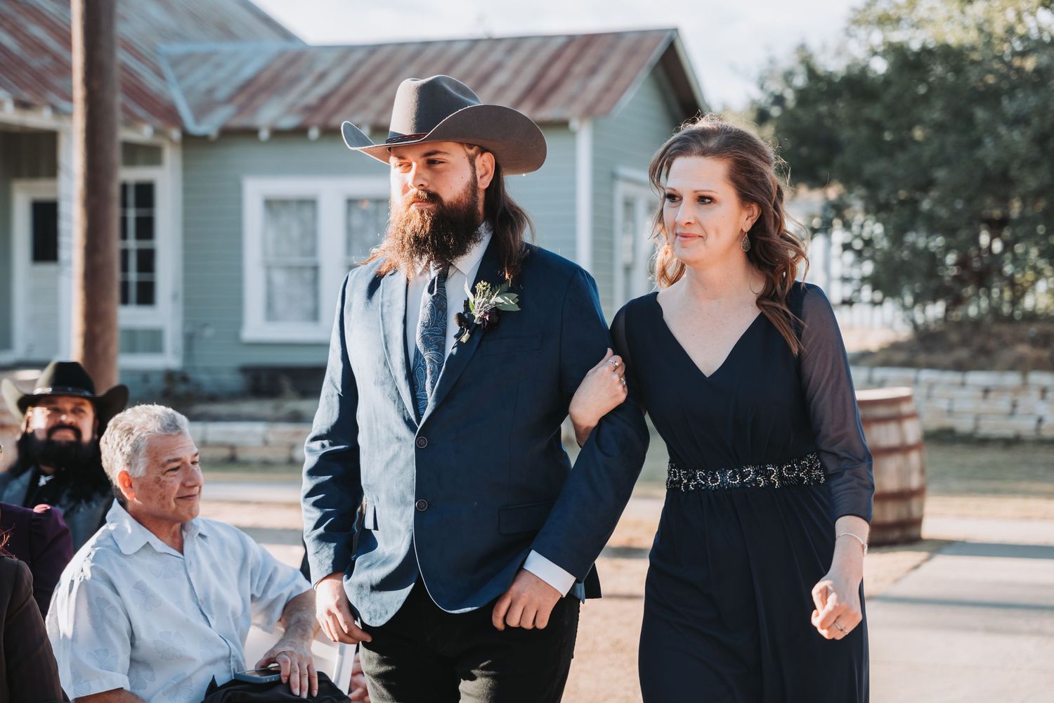 A couple walks with family members outside rustic buildings during a wedding celebration.
