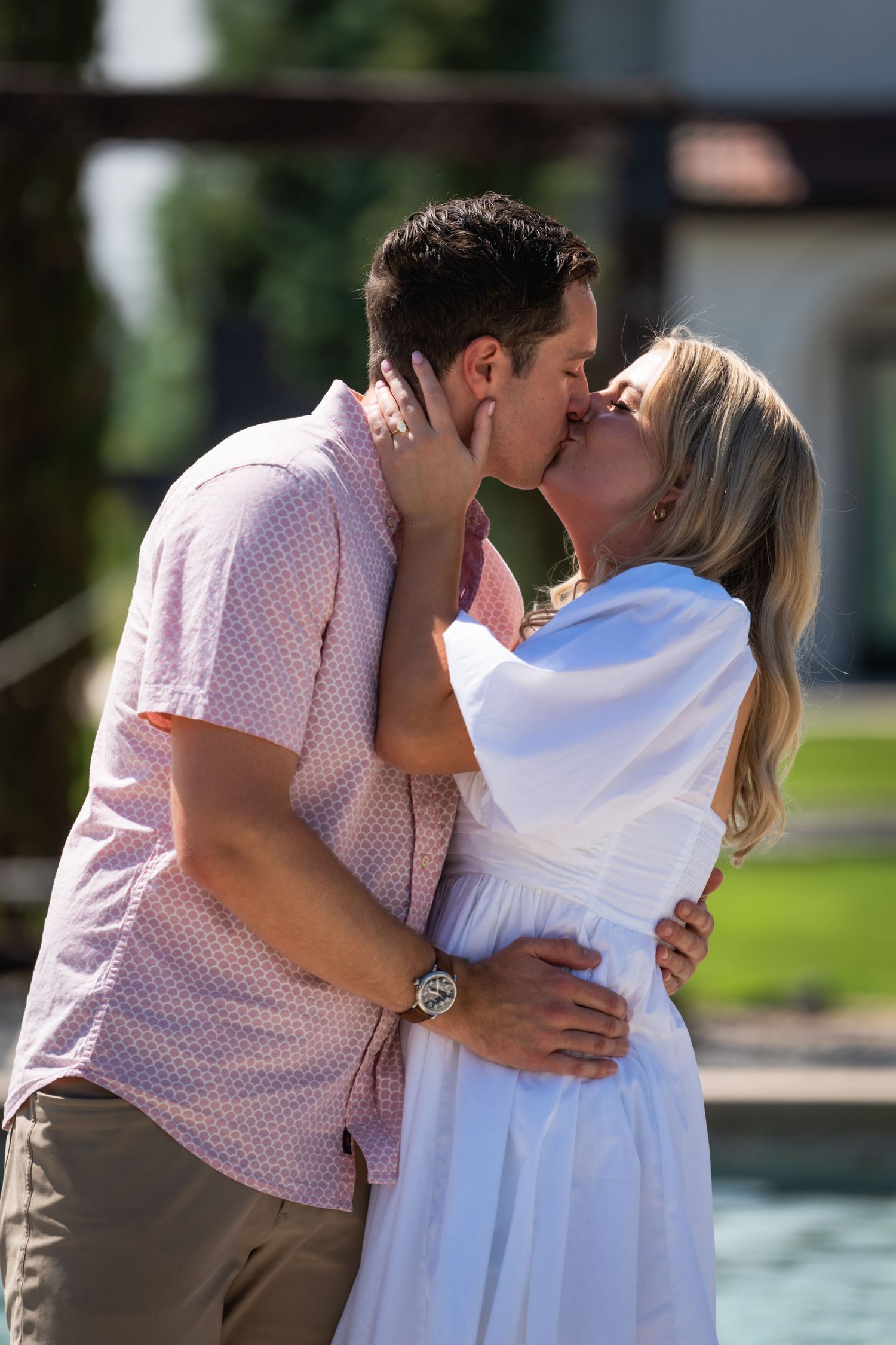 A romantic poolside kiss between a couple dressed in pink and white summer outfits.