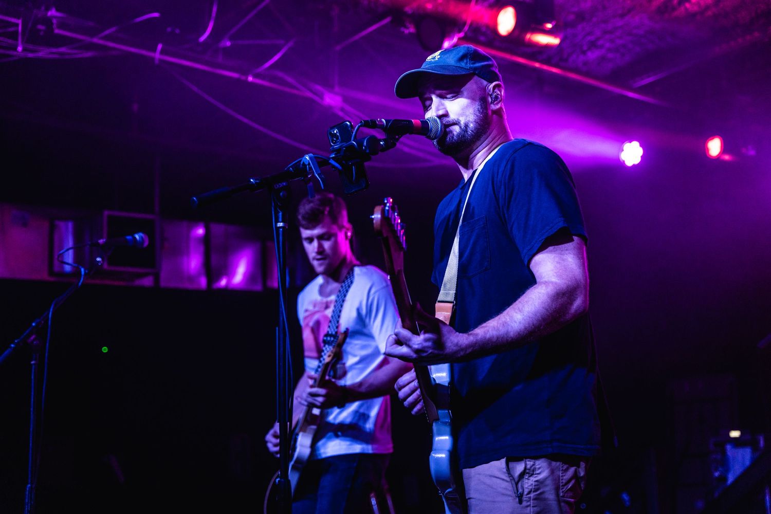 Musicians perform under dramatic purple stage lighting during intimate concert setting.