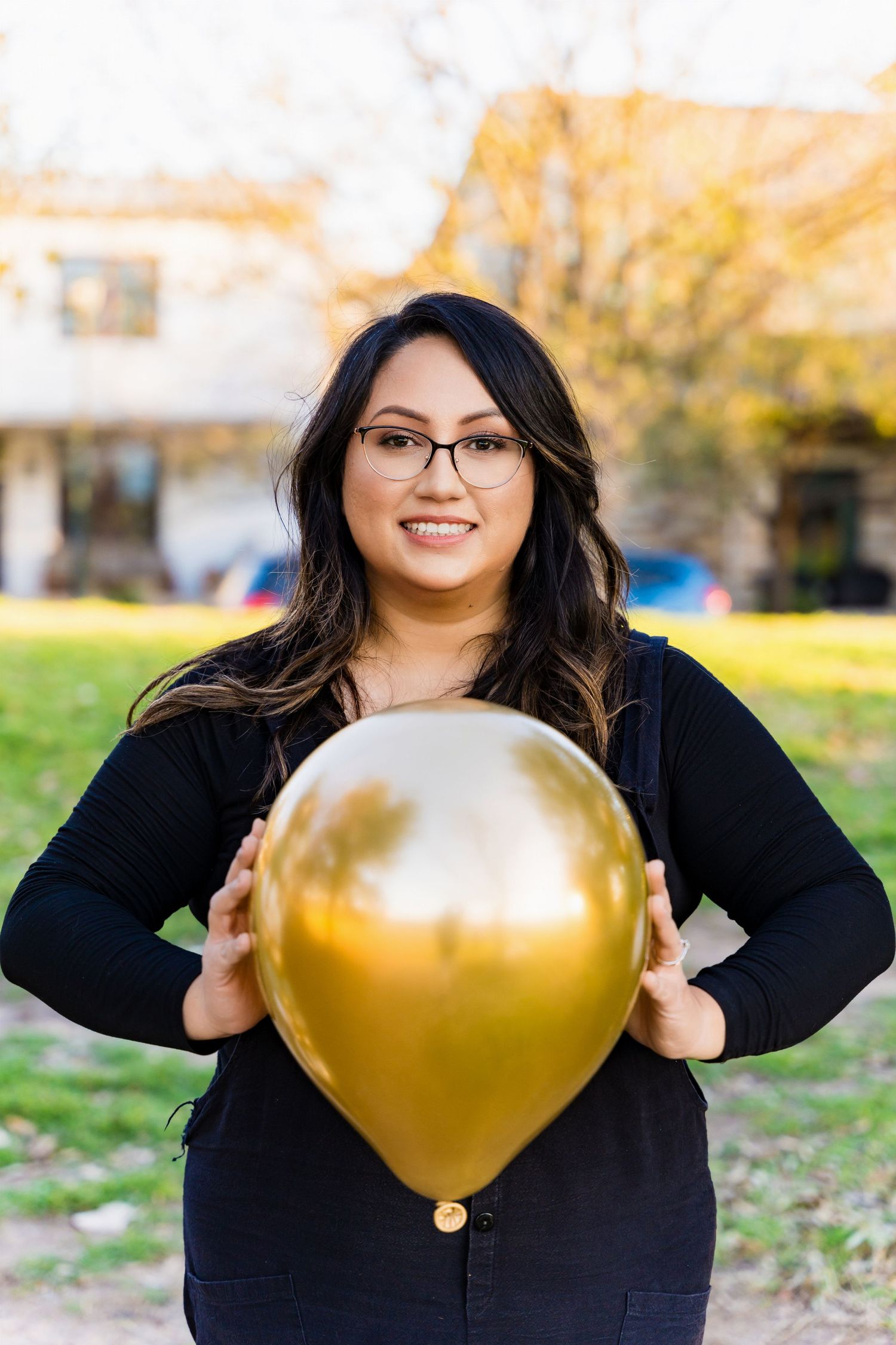 Person in black holding a large golden balloon while standing outdoors.
