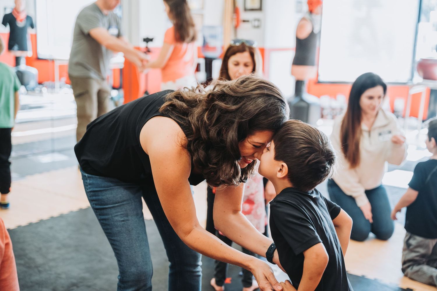 Trainer and student share a playful moment during martial arts class in orange-accented studio space.