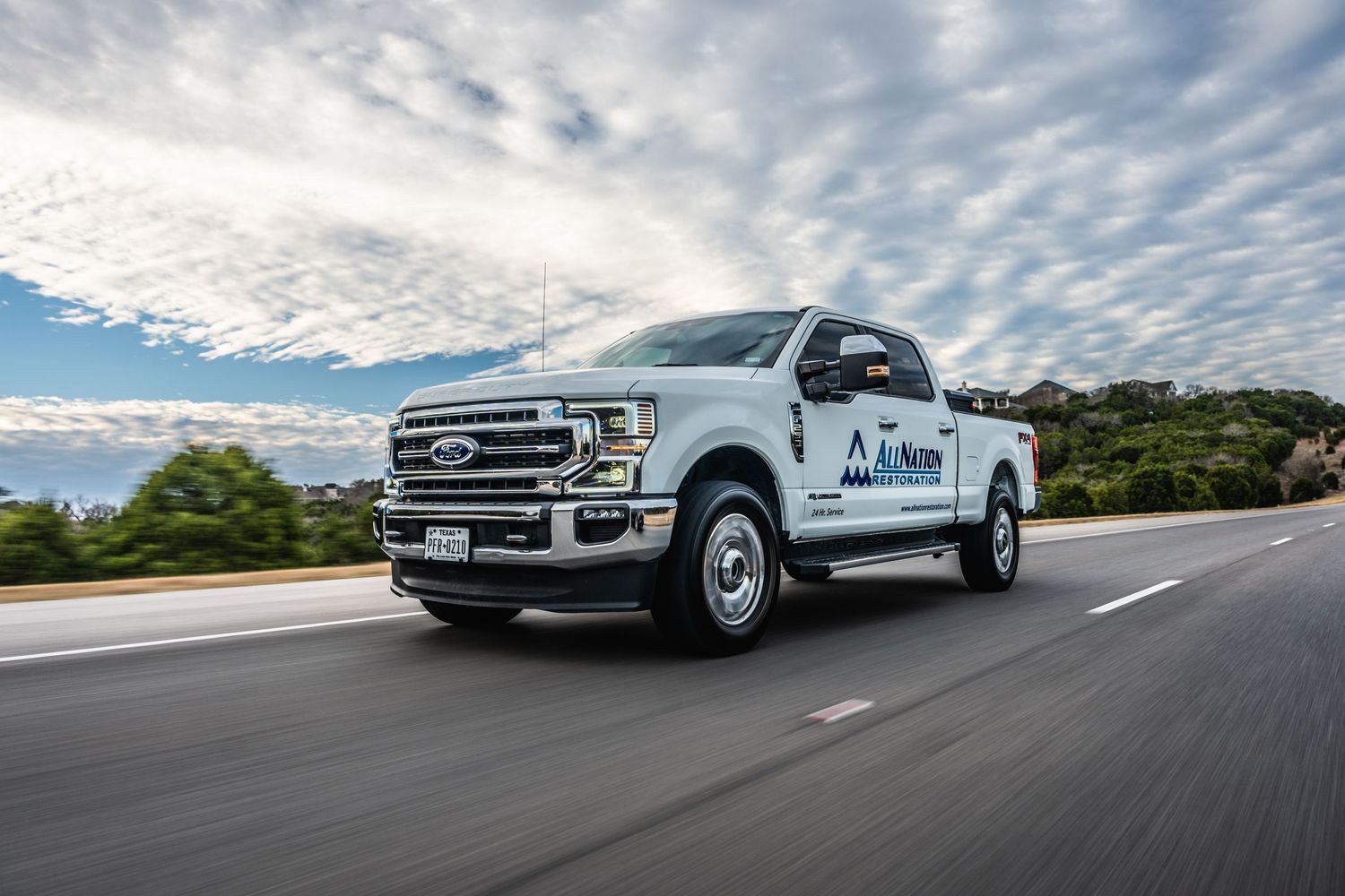 A white Ford F150 pickup truck driving on a road under dramatic cloudy skies.