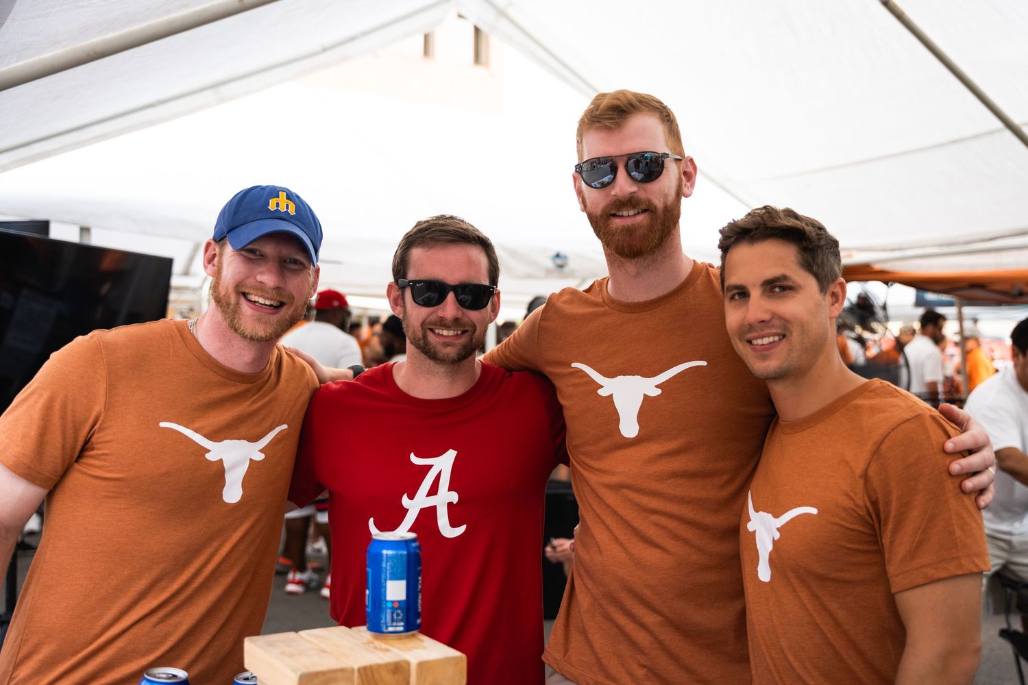 Four fans in Texas Longhorns and Alabama gear posing together at tailgate event.
