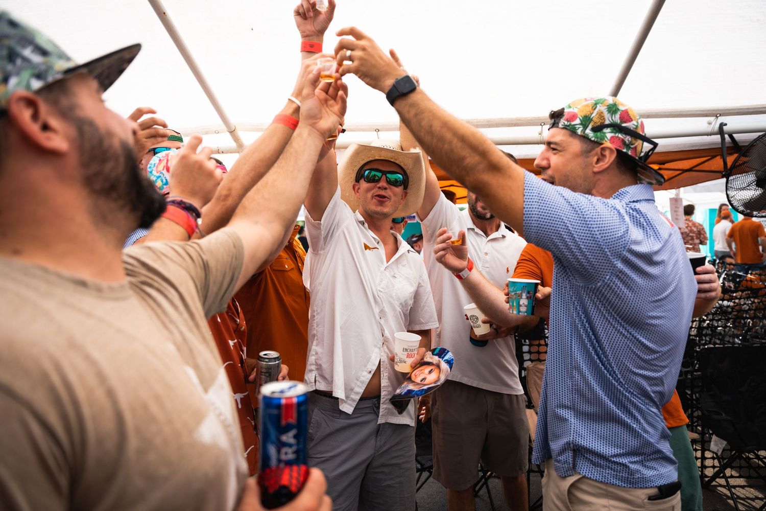 Group of fans in casual attire cheers and raises drinks during an outdoor celebration.