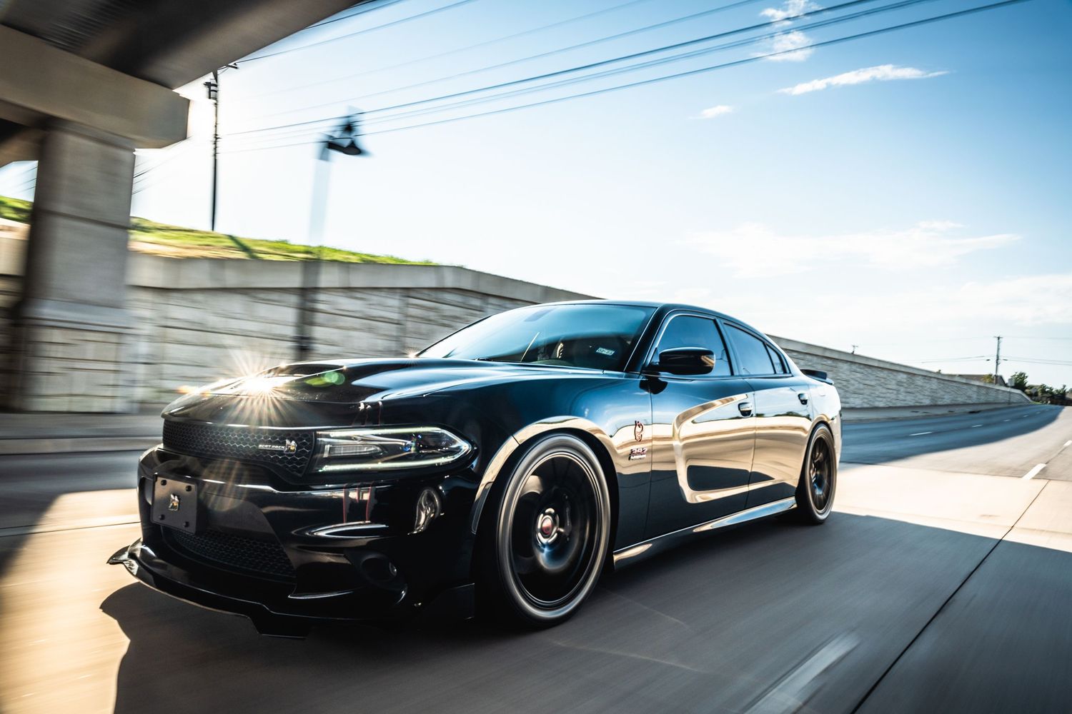 Black Dodge Charger photographed in motion near concrete overpass.