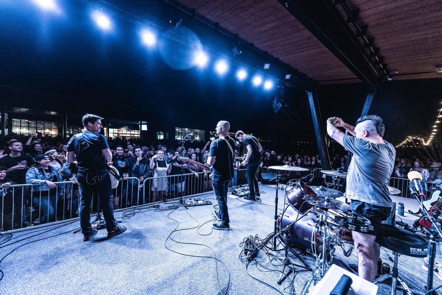 Wide shot of band performing on concert stage with crowd barrier and blue lighting.
