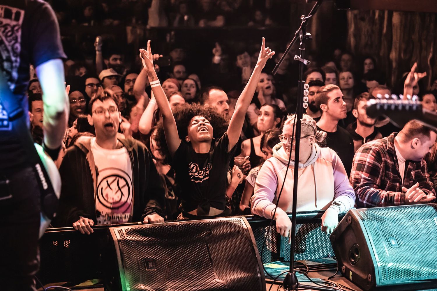 Energetic crowd raises hands at concert with band performing on stage.