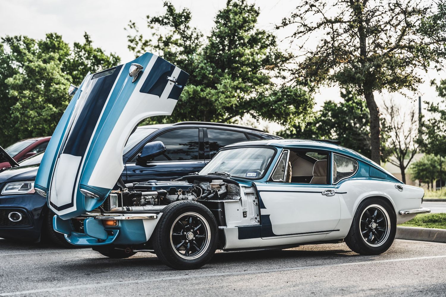 Classic light blue vintage sports car with hood open displaying custom engine modifications.