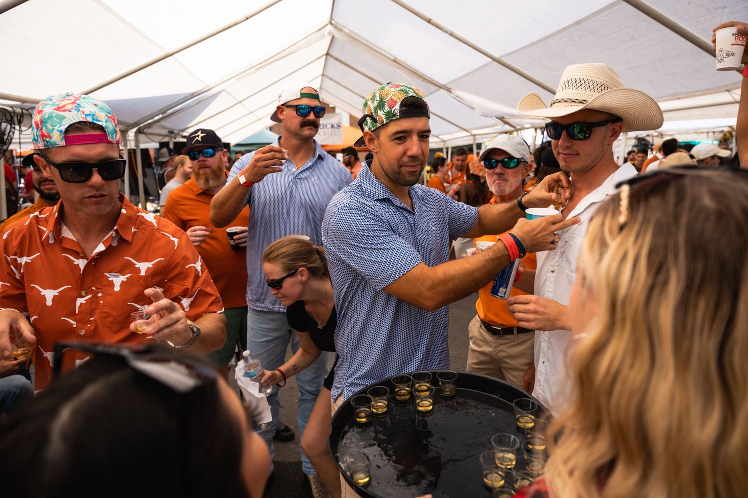 Crowd of sports fans gathered under a white tent for tailgating festivities.