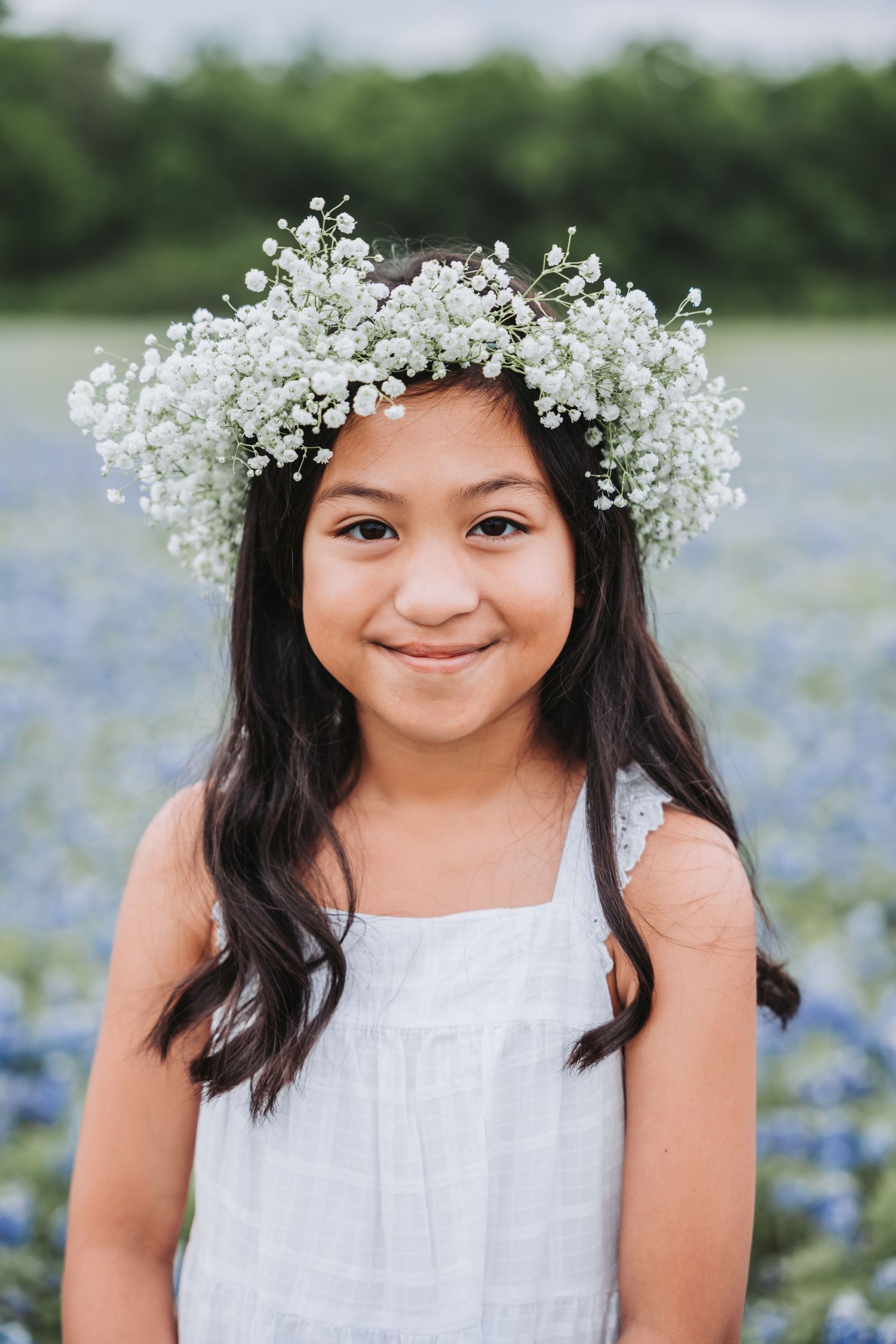 Figure wearing a baby's breath flower crown and white dress poses in a bluebonnet field.
