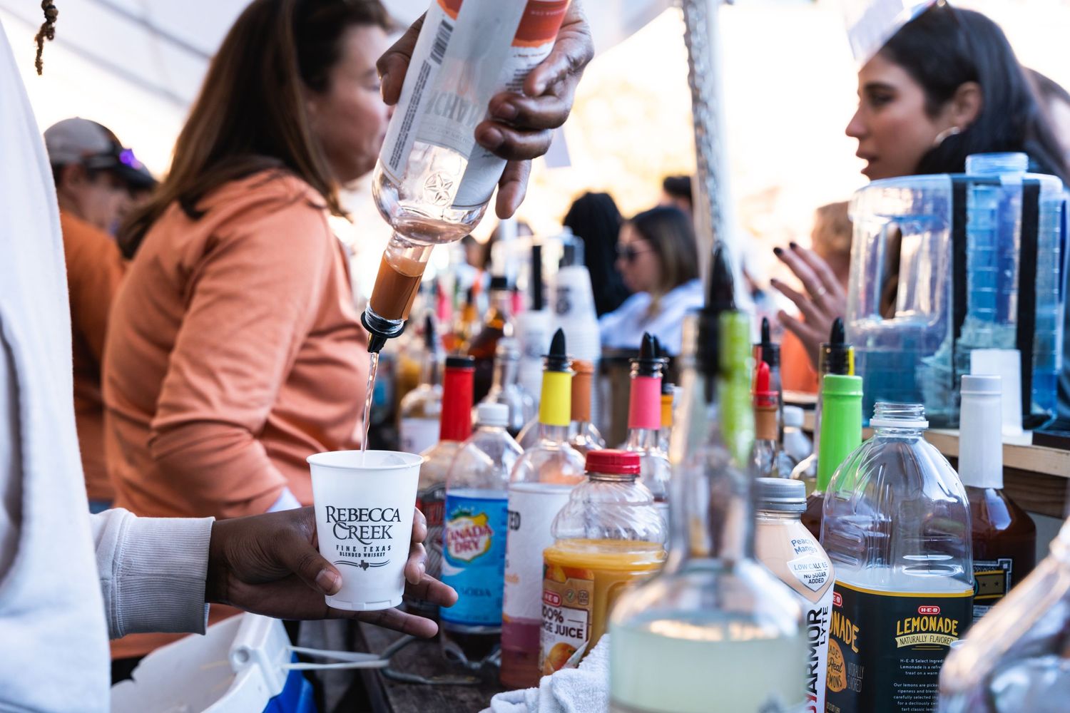 Beverages being poured at an outdoor bar setup under a white tent.