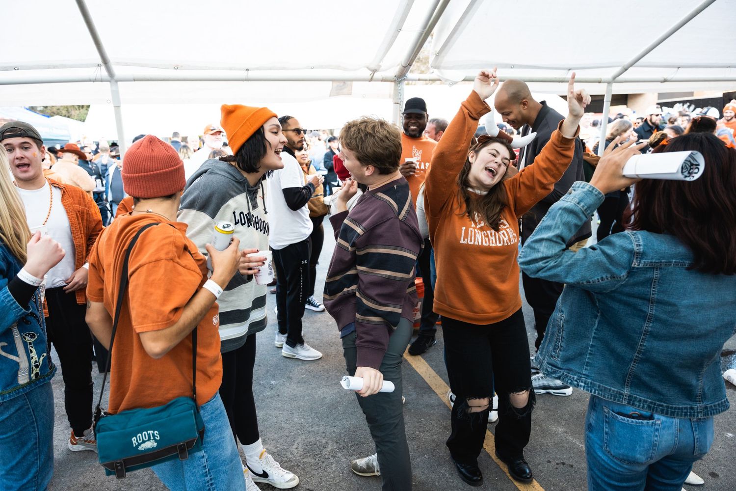 Enthusiastic students dancing and celebrating at an outdoor university event wearing team colors.